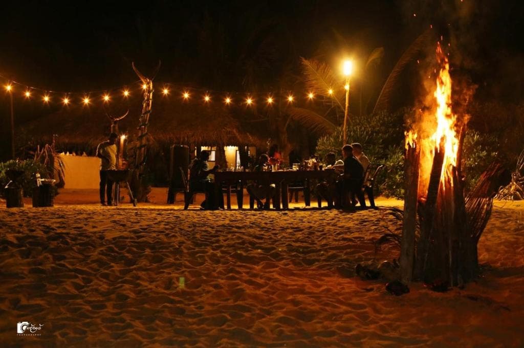 Guests dining by a bonfire under string lights on the beach
