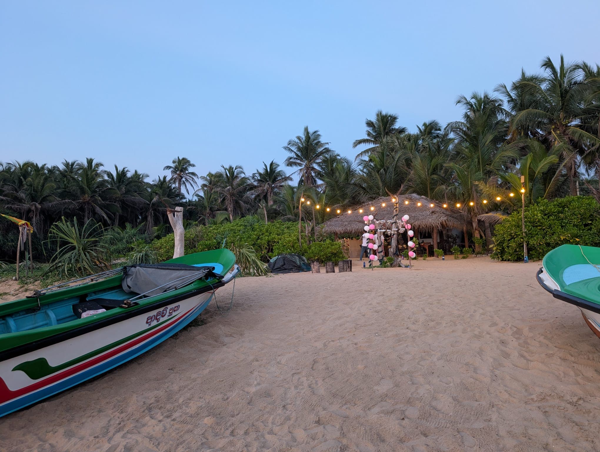Fishing boats on the sand before the lit beach restaurant at dusk