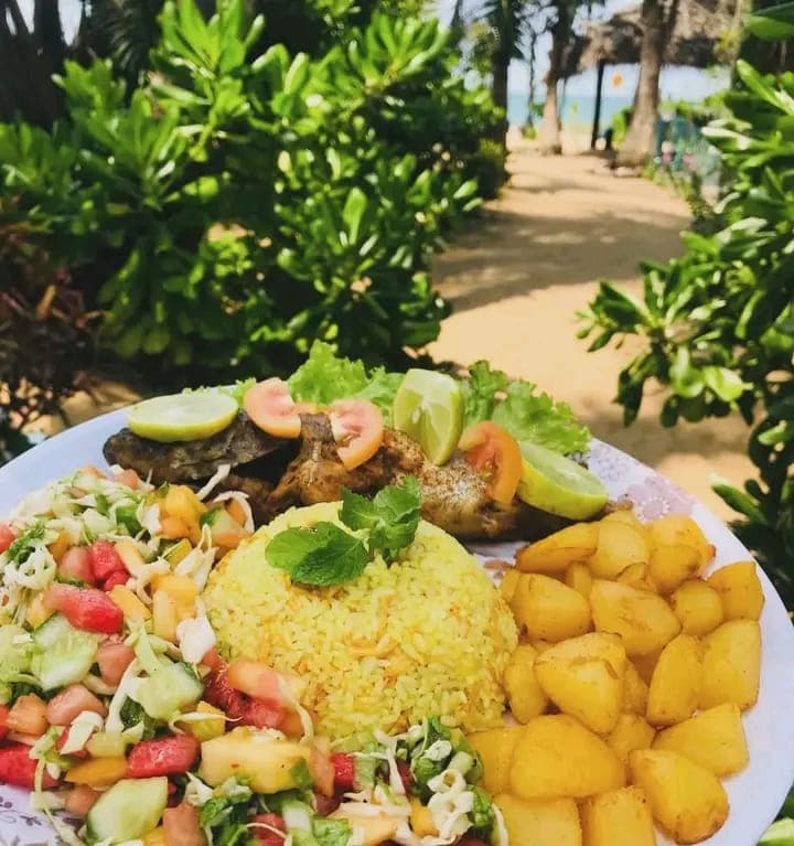 A plate of grilled fish with lime, tomato, yellow rice, salad and roast potatoes